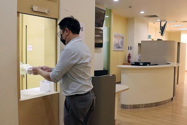  ​A hospital staff member demonstrating how a Covid-19 swab specimen is handed over to hospital staff for processing at the antigen rapid test centre at Singapore General Hospital.  PHOTO SINGAPORE GENERAL HOSPITAL