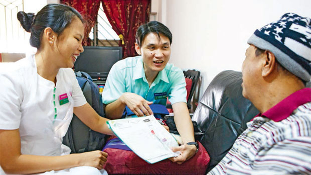  ​​During a home visit, Senior Staff Nurse Lee Zhao Yuan (extreme left, with Senior Nurse Clinician Jordan Hwang) checks Mr Haji Samad Siam’s overall health, including his temperature and blood pressure, before administering the chemotherapy drug via an injection.